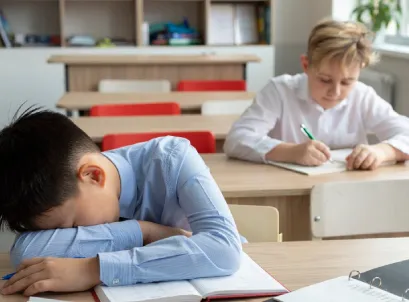 Child resting head on desk while classmate studies, illustrating ADHD or autism challenges