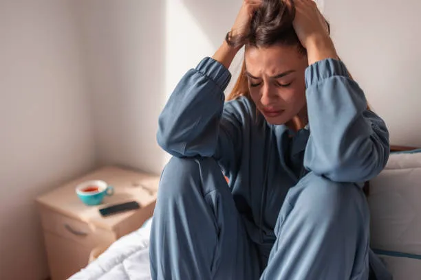 Woman sitting on bed holding her head, showing anxiety and emotional distress