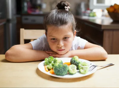 Child looking unhappily at plate of vegetables, illustrating childhood obesity concerns