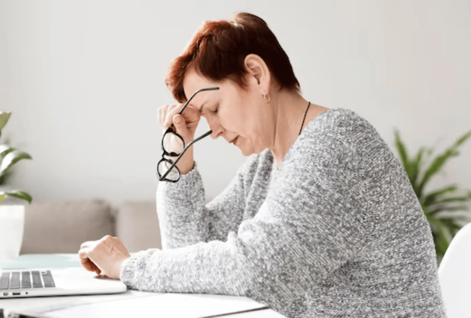 Stressed woman holding glasses at desk, illustrating cortisol stress hormone