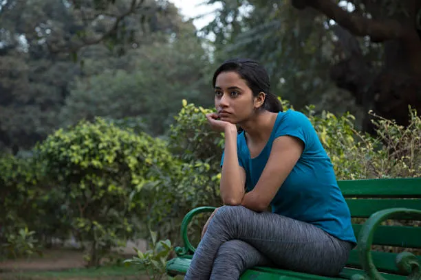 Woman sitting pensively on a park bench, appearing thoughtful or worried
