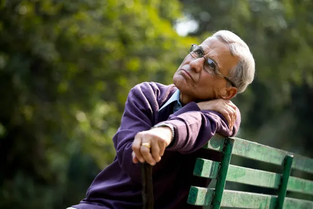 Elderly man sitting on park bench, looking thoughtful and reflective
