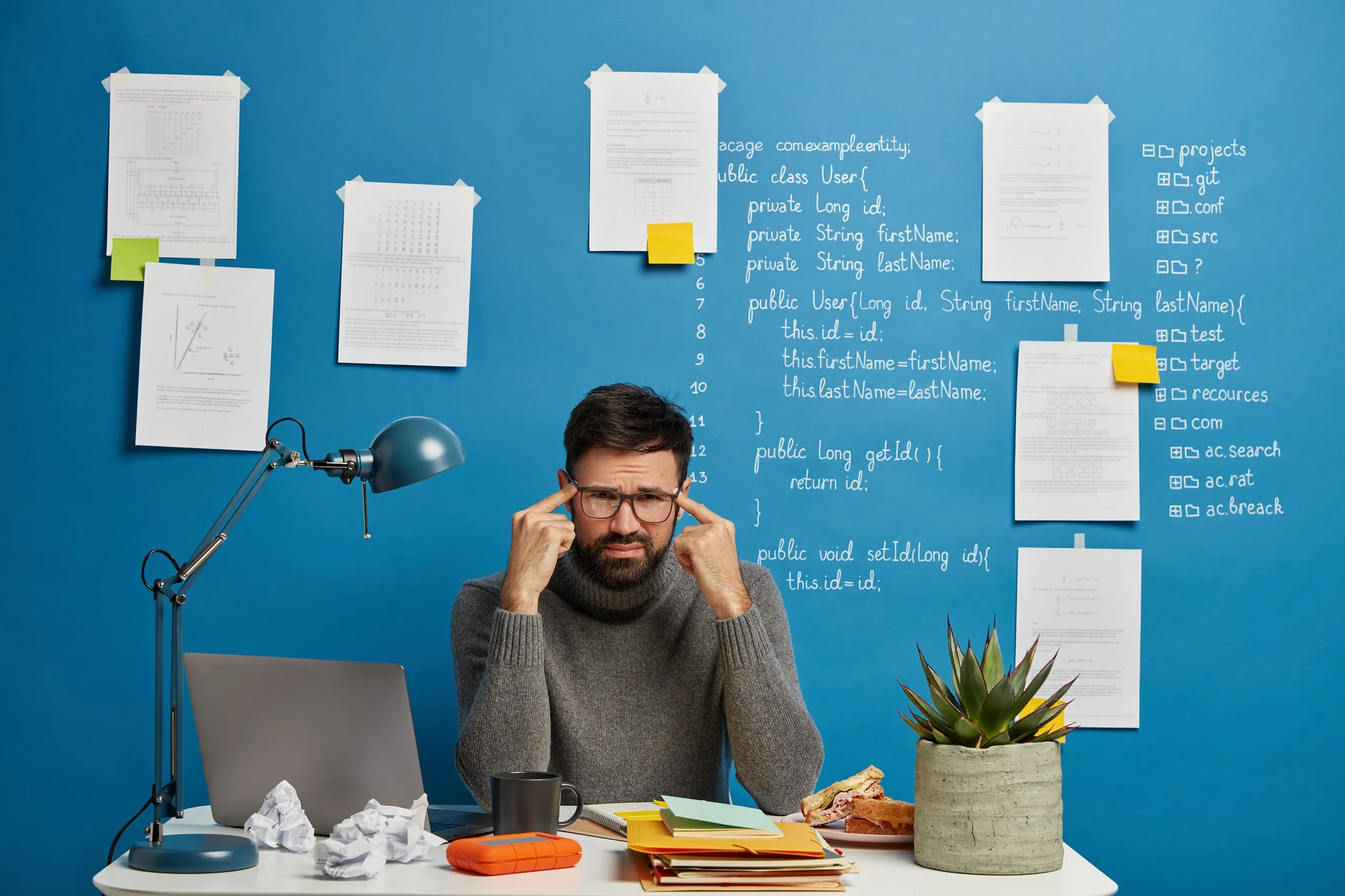 Man at cluttered desk holding temples, showing difficulty concentrating