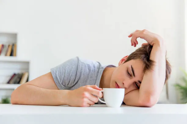 Exhausted man resting head on table holding coffee, showing rapid fatigue