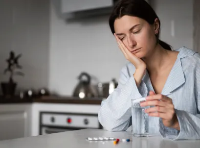 Woman with headache holding glass of water and pills, representing migraine discomfort