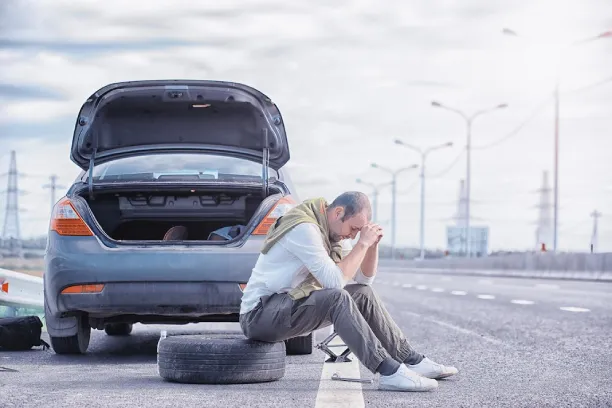 Man sitting by broken car on roadside, showing stress, worry, and frustration
