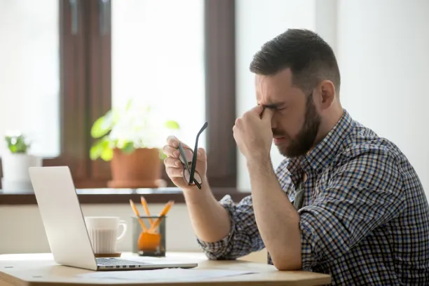 Man rubbing eyes at desk, showing eye strain, fatigue, or work stress
