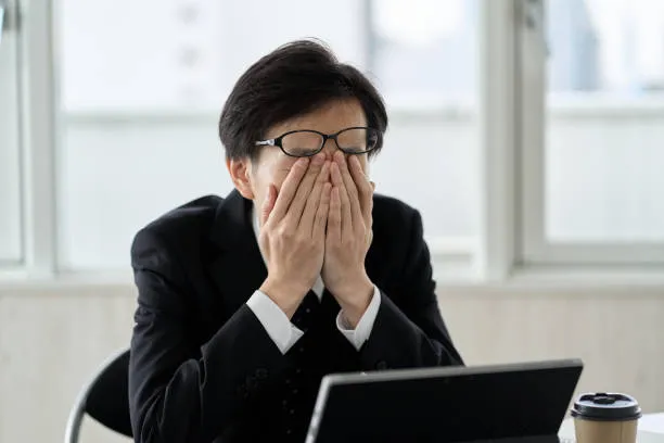 Tired professional covering face at desk, expressing restlessness and fatigue