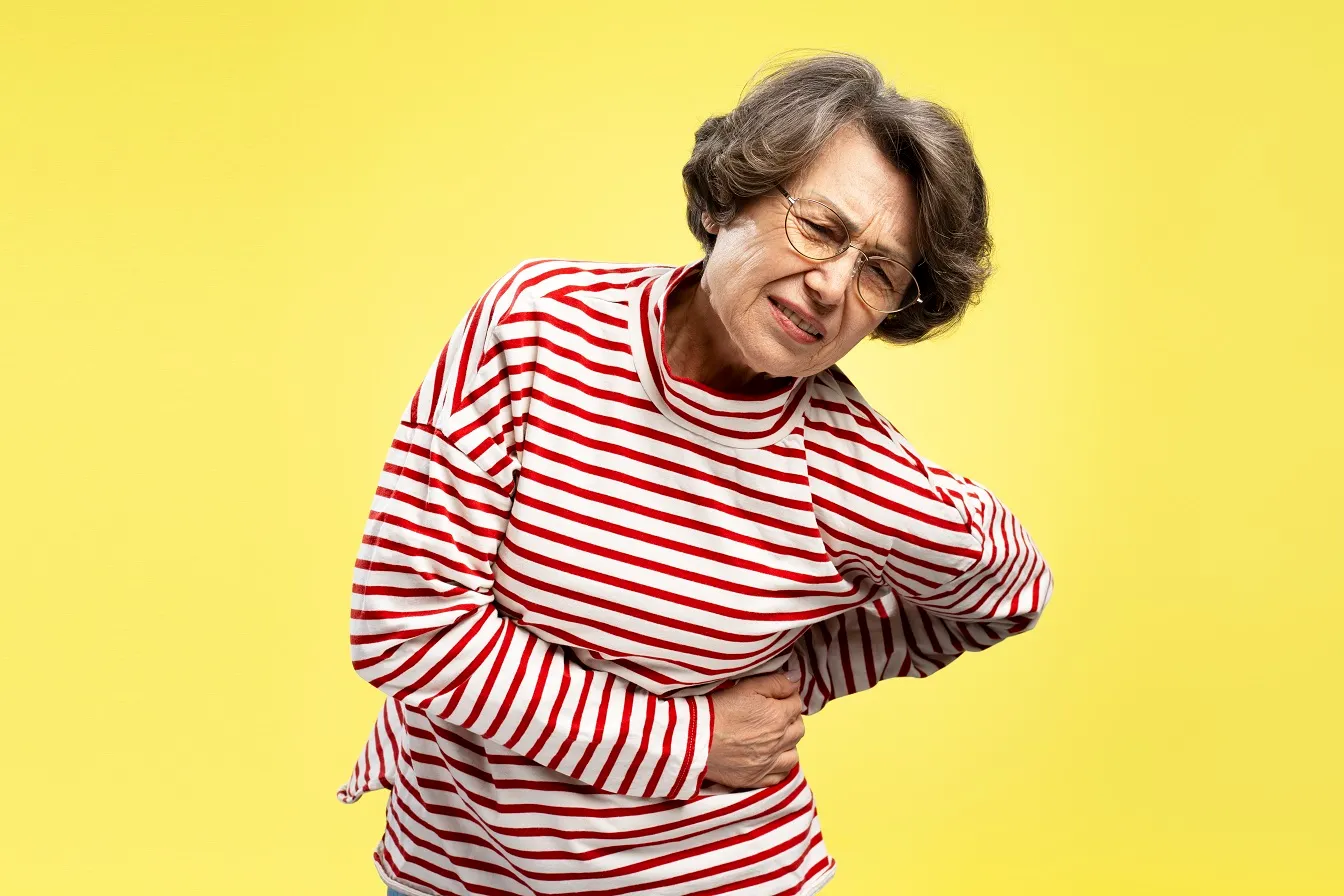 Elderly woman clutching her side in discomfort, expressing physical pain