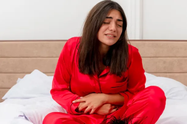 Woman in pajamas holding abdomen on bed, showing stomach pain or cramps
