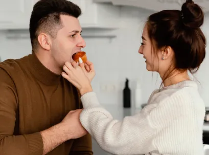 Woman feeding man fruit at home, playful moment suggesting shared healthy eating