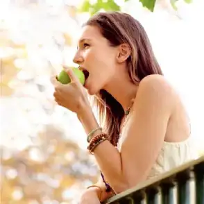 Woman eating a green apple outdoors, enjoying fresh fruit in sunlight
