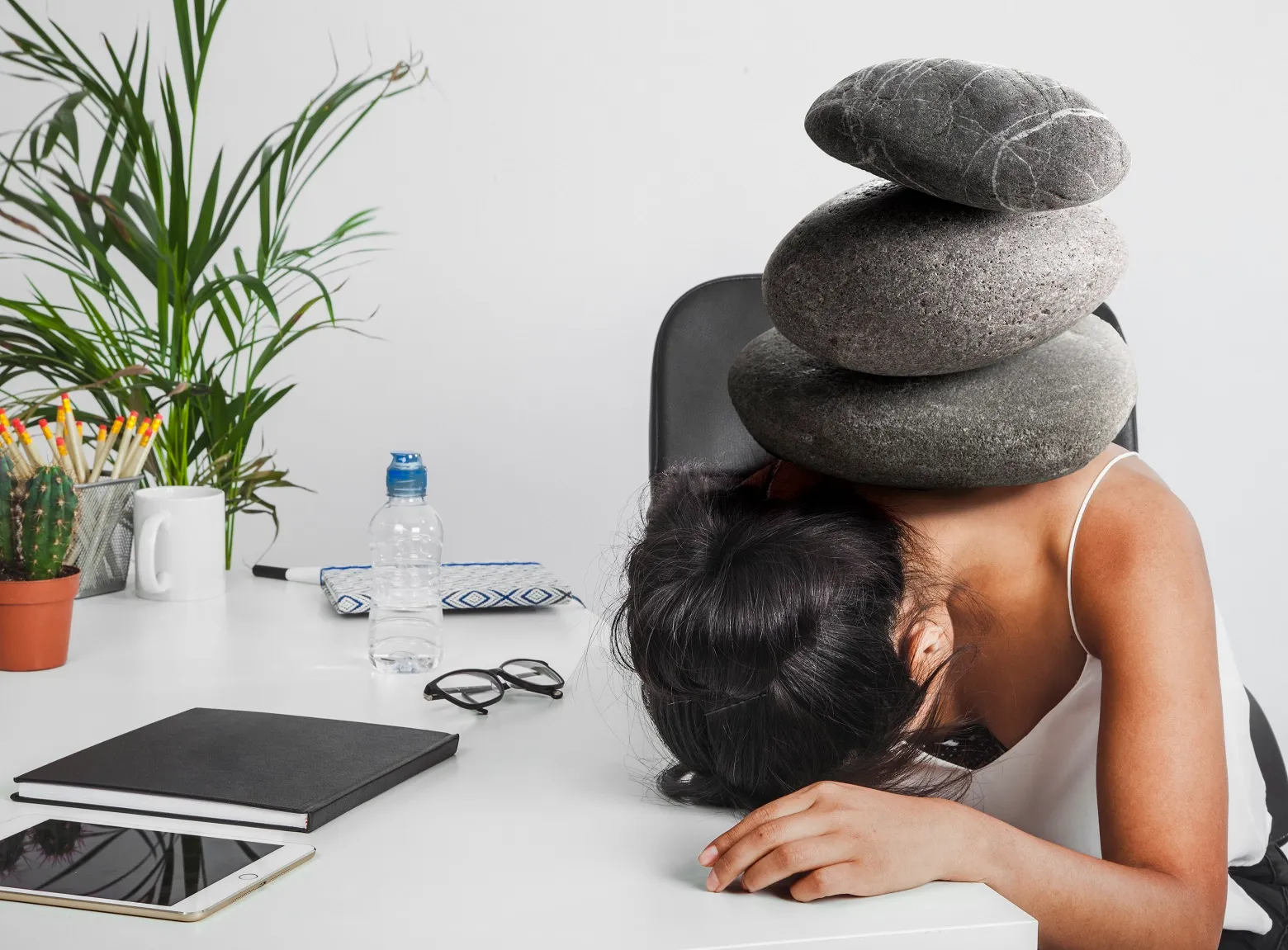 Woman resting head on desk with stacked stones, symbolizing depression