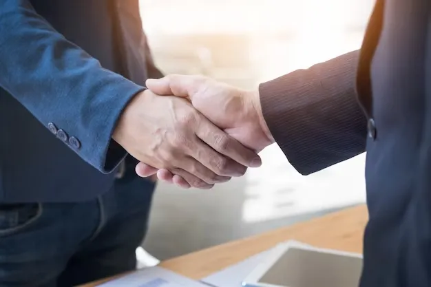 Business handshake across desk, symbolizing agreement, trust, and partnership
      