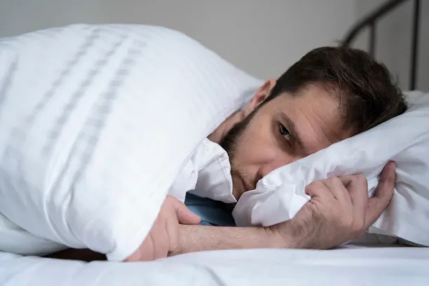Man lying awake in bed hugging pillow, showing difficulty sleeping