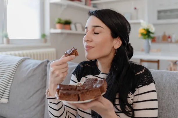 Woman enjoying chocolate cake, illustrating sugar cravings and comfort eating
