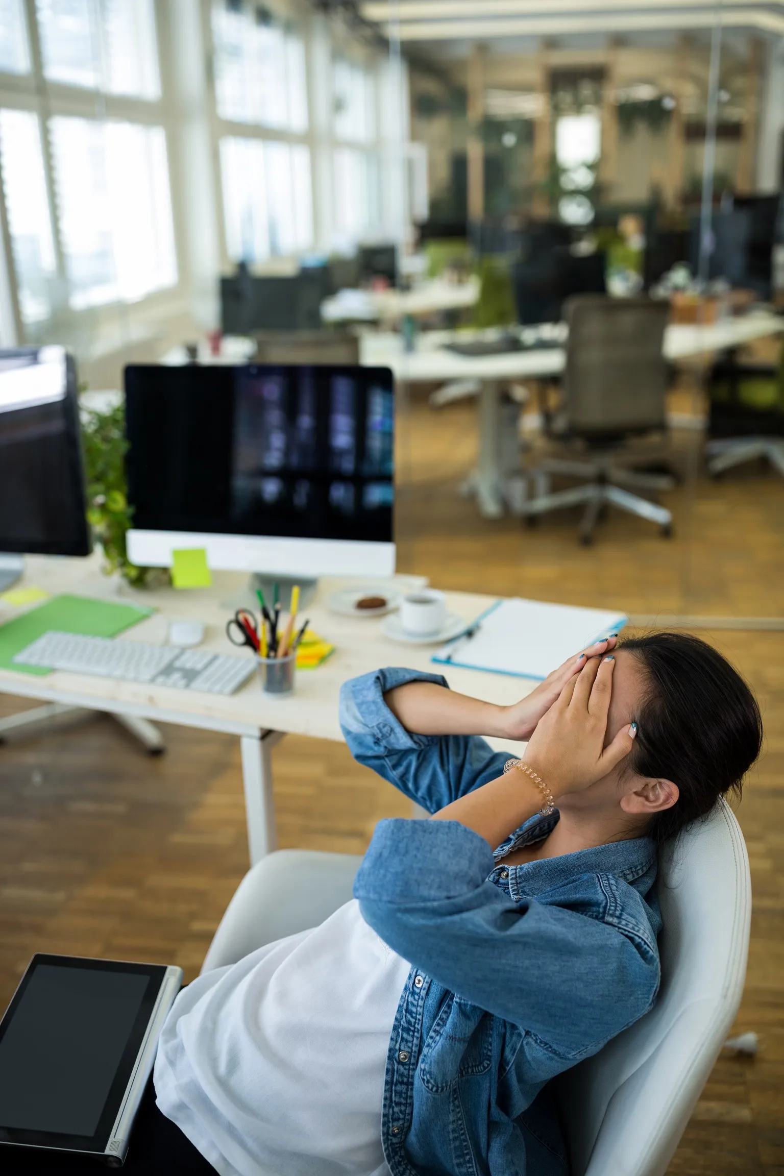 Office worker covering face at desk, showing stress and workplace burnout
